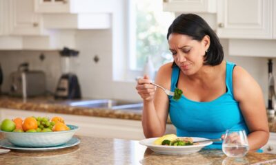 Mujer Sentada Al Mesón De La Cocina Mientras Come Un Plato De Ensalada Con Expresión De Disgusto. Medicamentos Como Ozempic Pueden Causar Incomodidad Al Comer Y Enfermedades Serias.