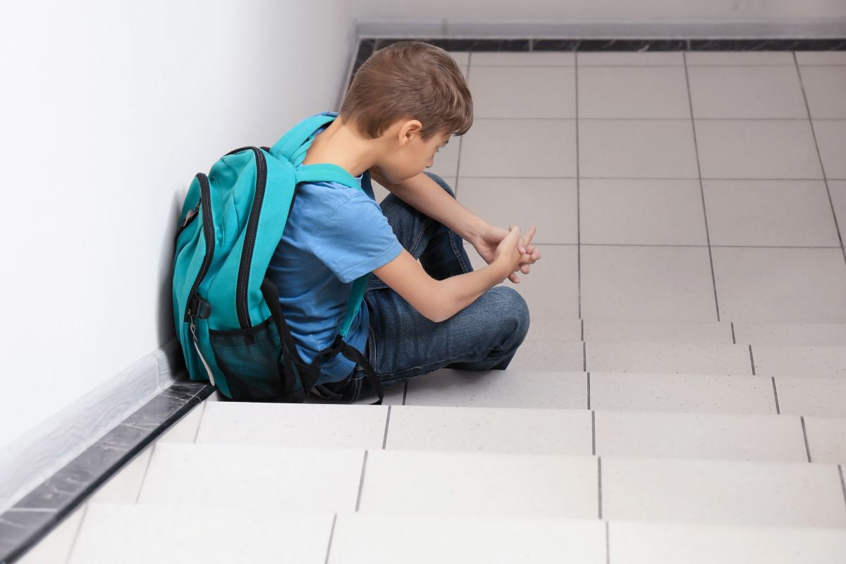 Clergy Abuse Sad adolescent boy sitting at the bottom of stairs with a backpack