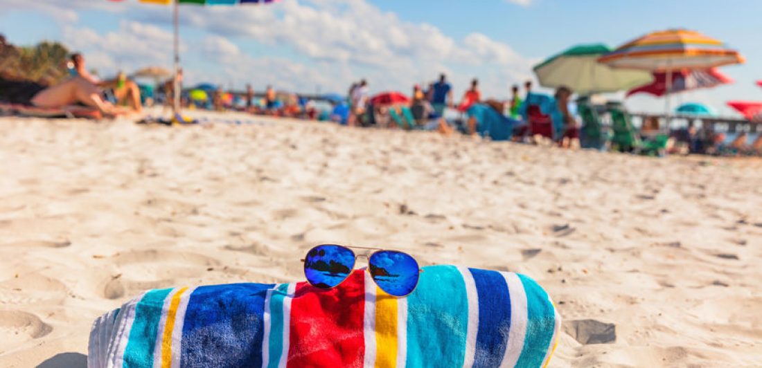 Beach towel and fashion sunglasses on Florida beach background -summer vacation travel concept copy space. Crowded popular USA destination for american holidays.
