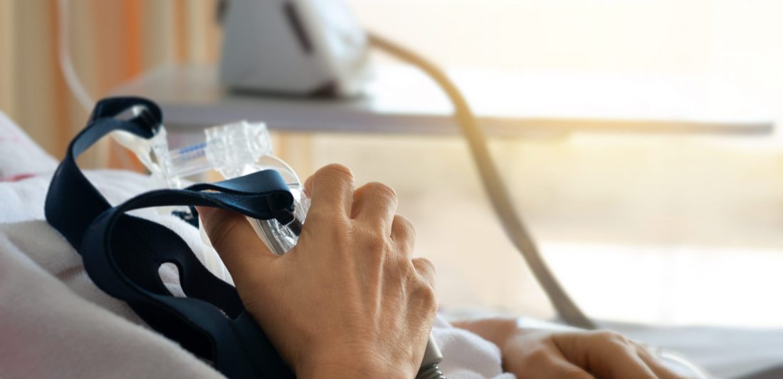 Close up of senior patient woman hand holding Cpap mask between the chest lying  in hospital room.
Obstructive sleep apnea therapy.